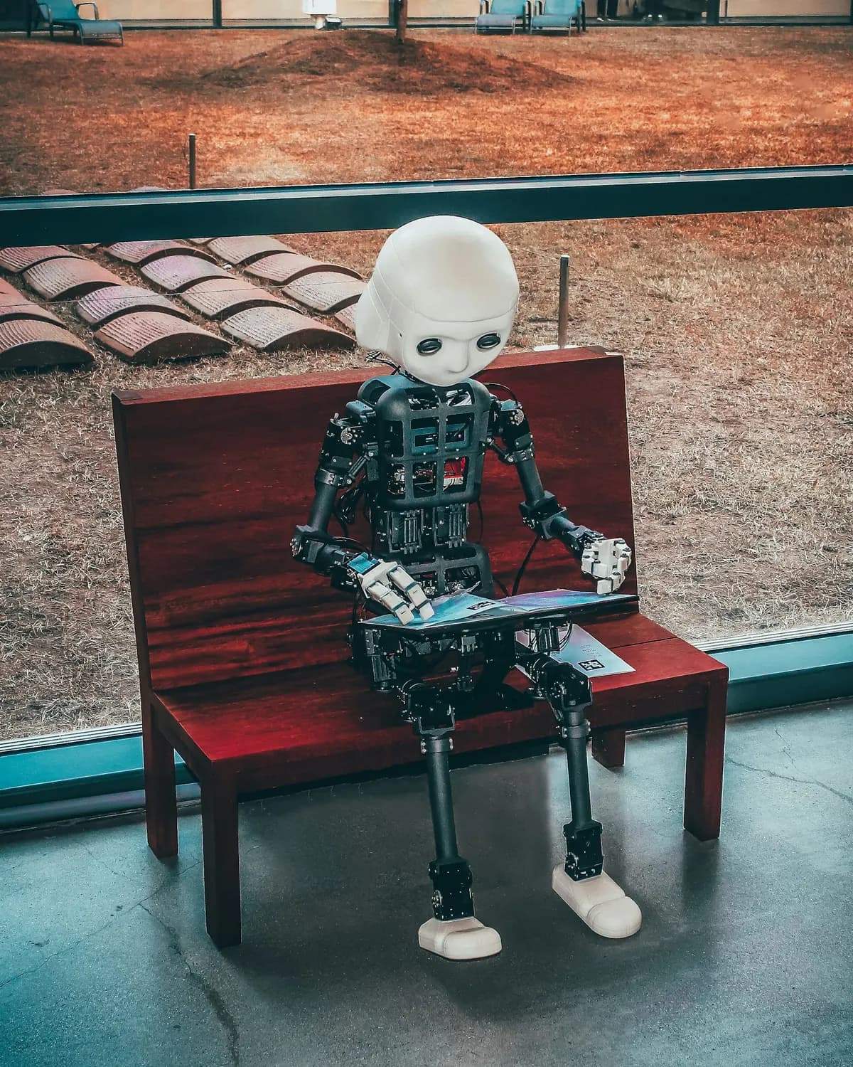 A small robot sitting at a bench working on a laptop